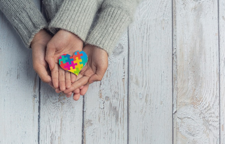 Na wyciągniętych dłoniach serce ułożone z kolorowych puzzli 